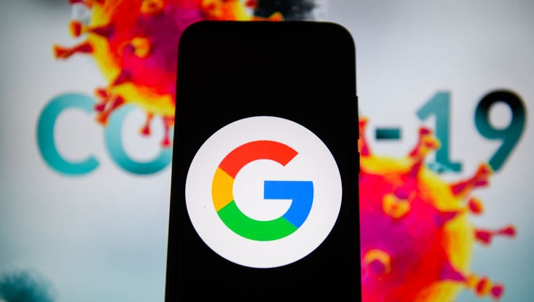 A Google logo is seen displayed on a smartphone with a COVID-19 sample on the background. 
