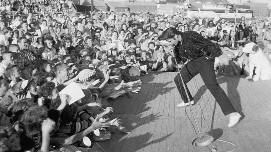 vers 1957 : le chanteur et acteur américain Elvis Presley (1935-1977) se produisant à l'extérieur sur une petite scène à l'adulation d'une jeune foule.  (Photo de Hulton Archive/Getty Images)