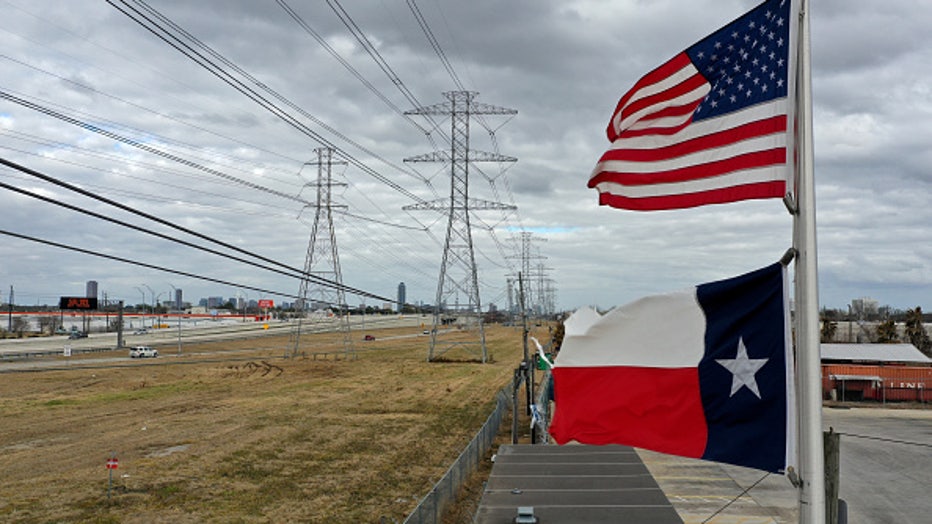 HOUSTON, TEXAS - FEBRUARY 21: The U.S. and Texas flags fly in front of high voltage transmission towers on February 21, 2021 in Houston, Texas. Millions of Texans lost power when winter storm Uri hit the state and knocked out coal, natural gas and nuclear plants that were unprepared for the freezing temperatures brought on by the storm. Wind turbines that provide an estimated 24 percent of energy to the state became inoperable when they froze. (Photo by Justin Sullivan/Getty Images)