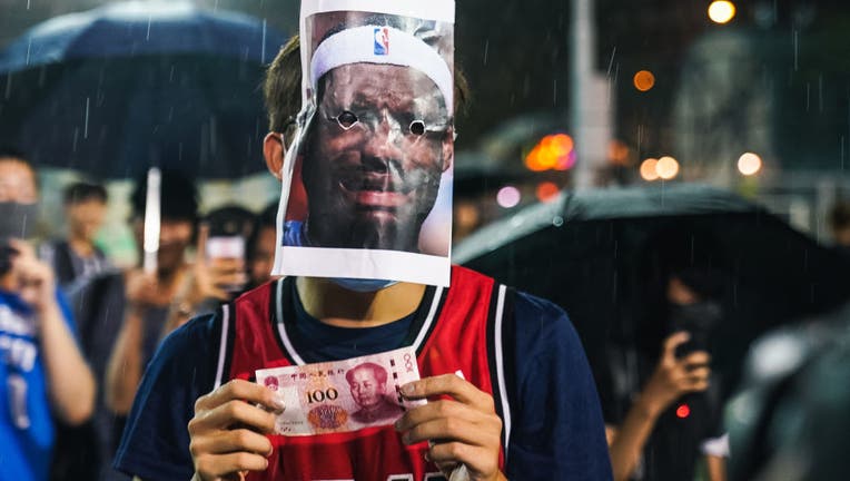 HONG KONG, CHINA: A basketball fan wearing Miami Heat jersey with a Lebron James mask on licking a 100 Chinese yuan bill on October 15, 2019 in Southorn Playground, Wan Chai, Hong Kong, China. Anti-government demonstrations in Hong Kong stretched into its fifth month after the Chinese territory's government invoked emergency powers earlier this month to introduce an anti-mask law. Protesters continue to call for Hong Kong's Chief Executive Carrie Lam to meet their remaining demands since the controversial extradition bill was withdrawn, which includes an independent inquiry into police brutality, the retraction of the word