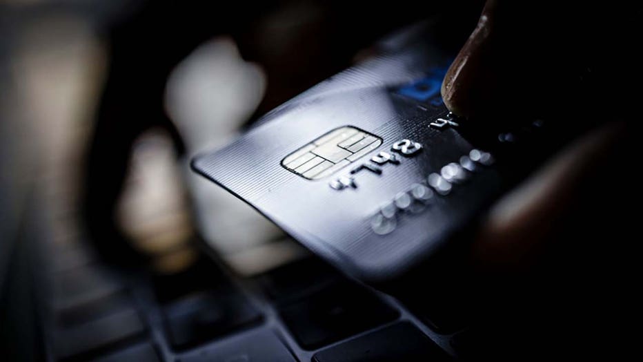 FILE - A credit card is held next to the keyboard of a laptop. (Photo by Thomas Trutschel/Photothek via Getty Images)