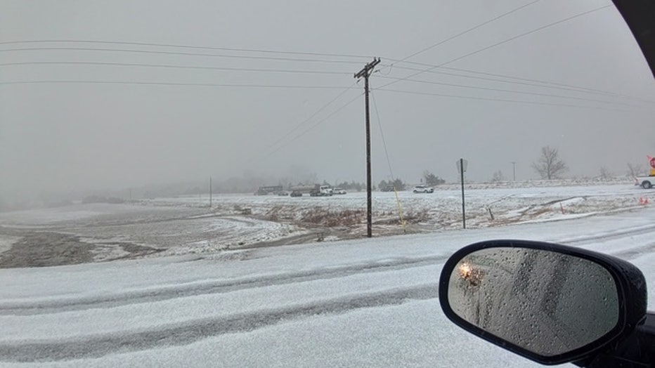 Hail-covered road out of a car window with a white sky and rearview mirror in the foreground