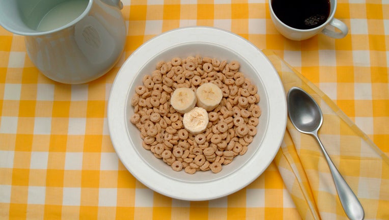 View of a table setting with a bowl of breakfast cereal (and banana slices), a cup of coffee, and a pitcher of milk, mid to late twentieth century.