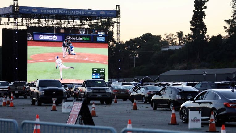 People in their vehicles watch the live baseball match between the Los Angeles Dodgers and Atlanta Braves at a parking lot of the Dodgers' stadium in Los Angeles, California
