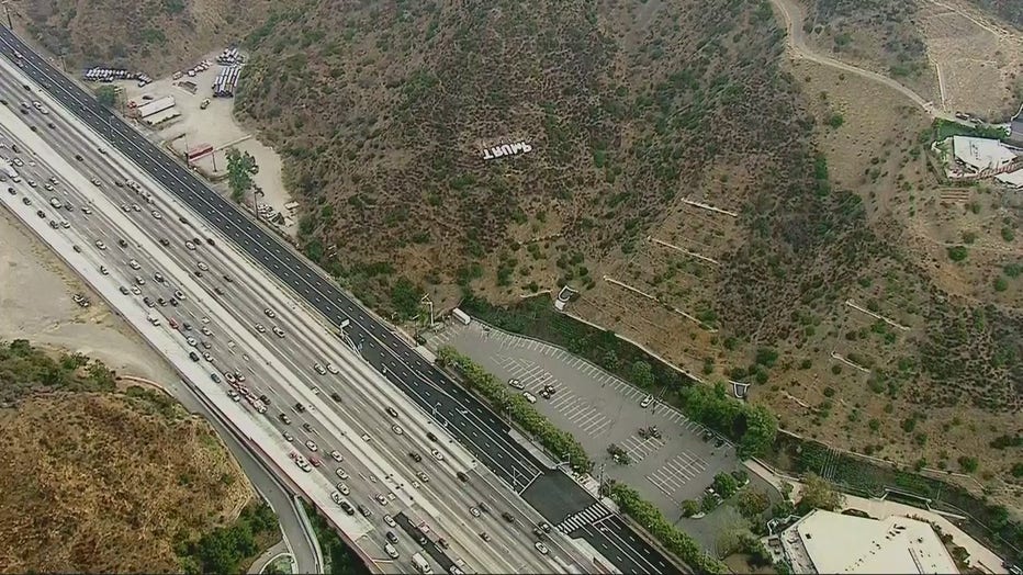 A large sign that read 'Trump' being removed from the hillside next to the 405 Freeway as cars drive past