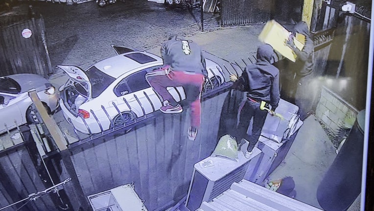 Thieves jumping a fence with boxes and bags