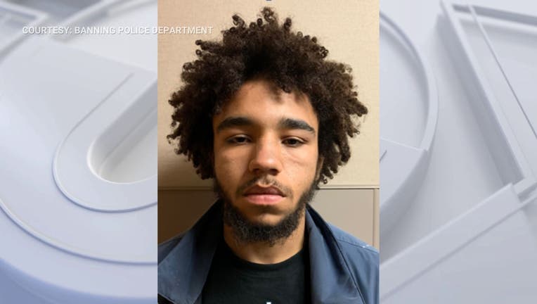 A mug shot of a shooting suspect wearing a black tshirt with a blue coat. The suspect has a mustache and beard, and curly black hair.