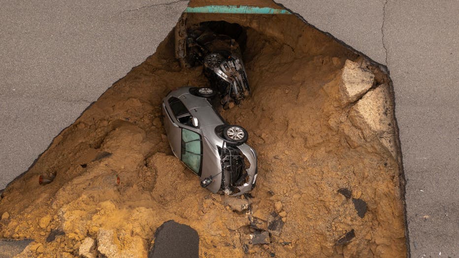 In an aerial view, a car and a pickup truck are seen inside a sinkhole as another storm created by a series of atmospheric rivers inundates California on January 10, 2023 in the suburban Los Angeles neighborhood of Chatsworth.