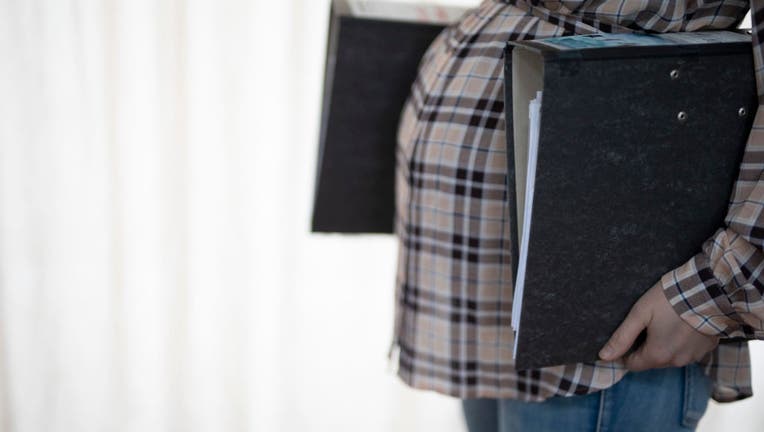 In this photo illustration a pregnant woman at work carries file folder. (Photo by Ute Grabowsky/Photothek via Getty Images)