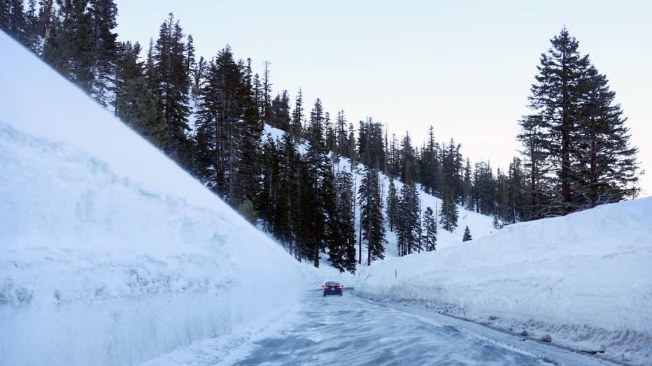 A car drives past snowbanks in the Sierra Nevada mountains on March 27, 2023 in Mammoth Lakes, California.