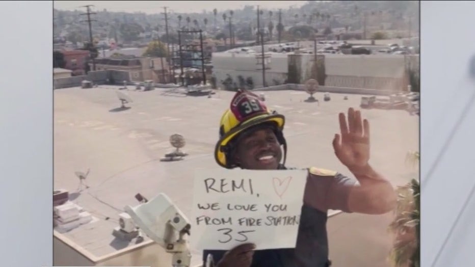 Firefighter Zane Archer holds a sign up to the window at Children's Hospital Los Angeles that reads, "Remi, we love you. From Fire Station 35."