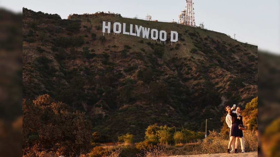 People take selfies beneath the Hollywood sign in Los Angeles