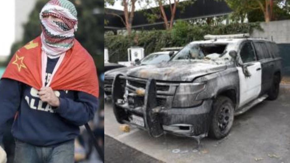 A Los Angeles protester wearing a face covering, wrapped in a flag, holding a large stone, next to a damaged and burned California Highway Patrol vehicle.