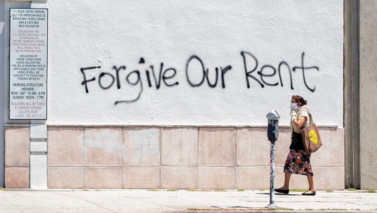 A woman wearing a mask walks past a wall bearing graffiti asking for rent forgiveness on La Brea Avenue amid the COVID-19 pandemic on May 1, 2020, in Los Angeles, California.