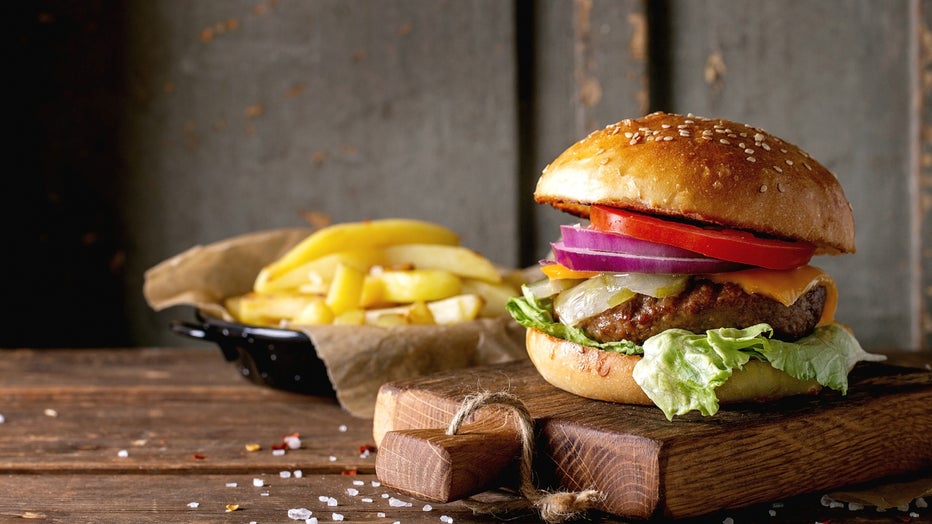 Fresh homemade burger on little cutting board with grilled potatoes. served with ketchup sauce and sea salt over wooden table with gray wooden background. Dark rustic style.