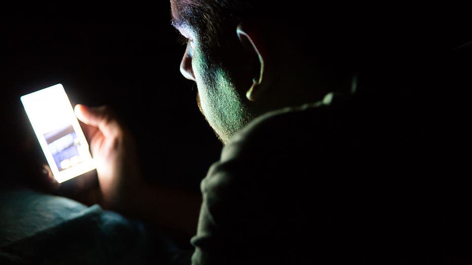 FILE - Man lying on a bed at night in a dark room checking his smartphone. (Credit: Getty Images)