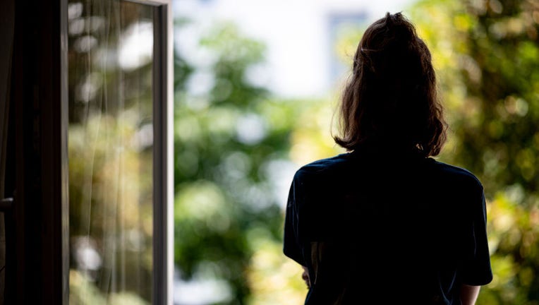 FILE - A young woman stands at a window in her home. (Photo by Fabian Sommer/picture alliance via Getty Images)