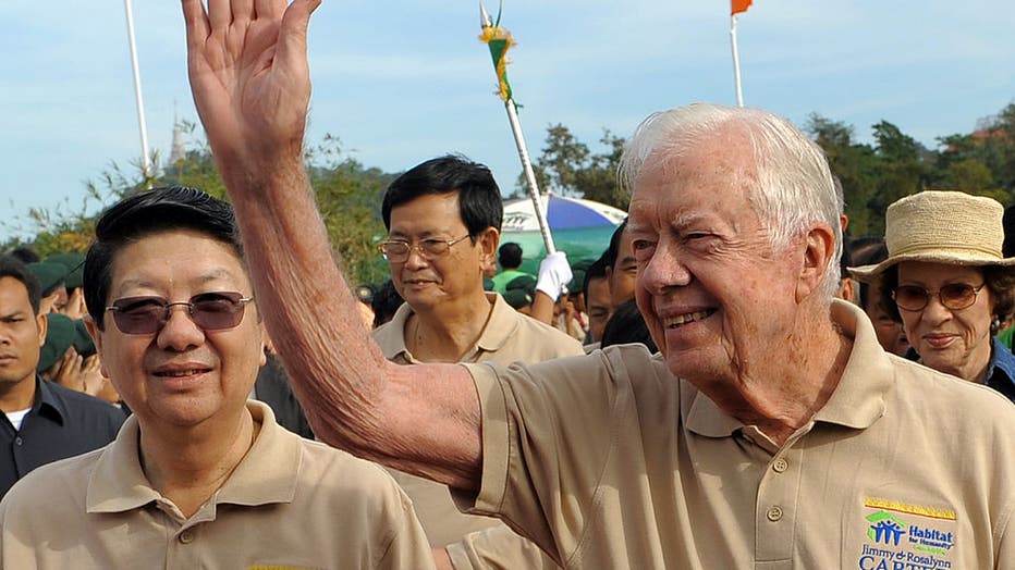 Former US president Jimmy Carter (R) waves as Cambodian Deputy Prime Minister Sok An (L) smiles during a ceremony to inaugurate a new housing project in Oudong, Kandal province, some 50 kilometers north of Phnom Penh on November 21, 2009. The volunteers for Habitat for Humanity built or repaired 166 homes in Cambodia, China, Laos, Thailand and Vietnam during a November 15-20 tour, the Atlanta-based Christian group said. (TANG CHHIN SOTHY/AFP via Getty Images)