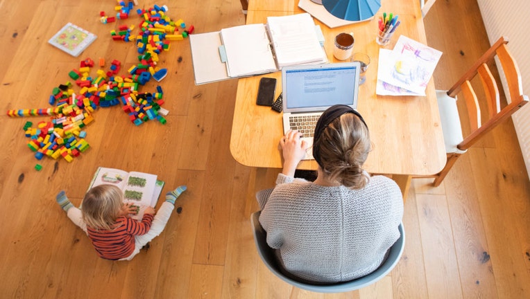 FILE - A toddler plays in the living room while his mother works on a laptop in the home office in a file image dated Jan. 20, 2021. (Photo by Julian Stratenschulte/picture alliance via Getty Images)