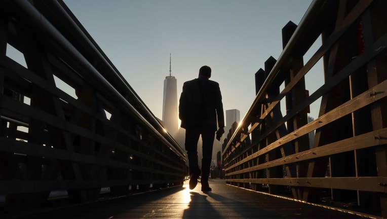 FILE - A commuter walks to a waiting ferry to New York City as the sun rises behind lower Manhattan and One World Trade Center on Sept. 20, 2022, in Jersey City, New Jersey. (Photo by Gary Hershorn/Getty Images)