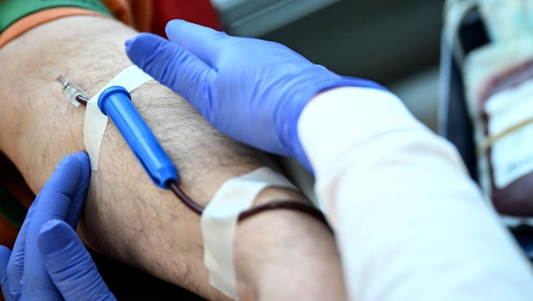 FILE - A needle with a tube is stuck in a mans arm at a blood drive. (Photo by Britta Pedersen/picture alliance via Getty Images)