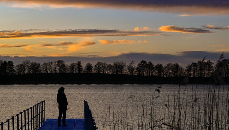 FILE - In the backlight of the setting sun, a woman stands on a dock overlooking a lake in a file image dated March 13, 2023. (Photo by Patrick Pleul/picture alliance via Getty Images)