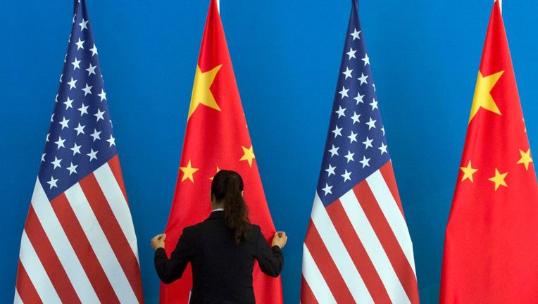 FILE - A Chinese woman adjusts a Chinese flag near US flags before the start of a Strategic Dialogue expanded meeting between China and the US during the US-China Strategic and Economic Dialogue held at the Diaoyutai State Guesthouse in Beijing on July 10, 2014. (Photo by NG HAN GUAN/POOL/AFP via Getty Images)