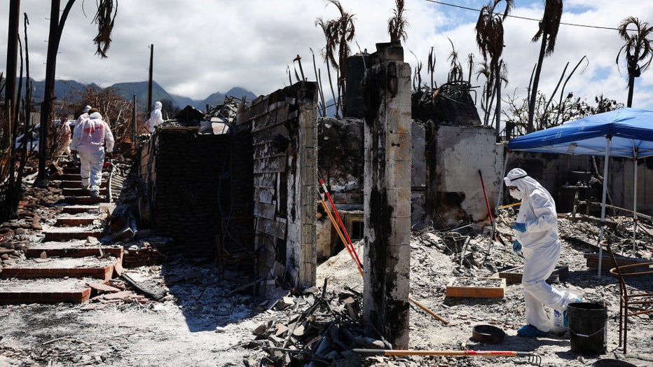 A displaced resident (R) walks while searching for personal items in the rubble of the wildfire destroyed home where she lived, as volunteers from Samaritan's Purse assist (L) on Oct. 5, 2023, in Lahaina, Hawaii. (Photo by Mario Tama/Getty Images)