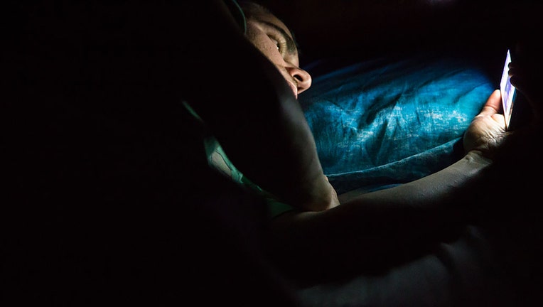 FILE - A man lying in bed late at night and scrolling on his smartphone. (Credit: Getty Images)