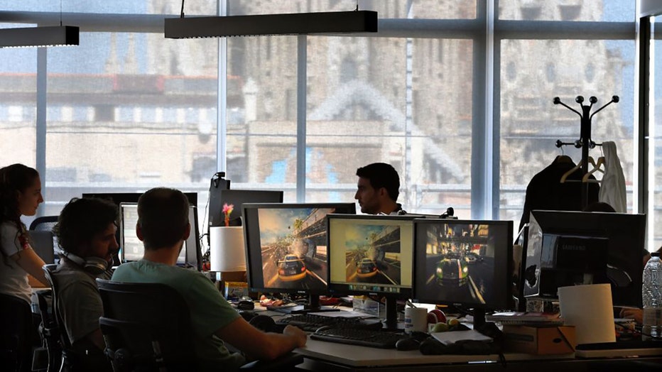FILE - Employees of French video game developer Gameloft work on their computers during a visit to the companys studios of Barcelona with the Sagrada Familia in background on Sept. 5, 2017. (Photo by LLUIS GENE/AFP via Getty Images)
