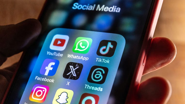 FILE - In this photo illustration, a man holds a smartphone iPhone screen showing various social media apps including YouTube, TikTok, Facebook, Threads, Instagram and X on March 13, 2024. (Photo by Anna Barclay/Getty Images)