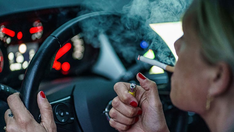 FILE - A woman lights a cigarette behind the wheel of her car. (Photo by Axel Heimken/picture alliance via Getty Images)