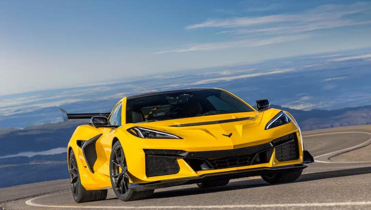 Mobil sport Corvette ZR1 tahun 2025 berwarna kuning melaju di jalan berliku dengan latar belakang pegunungan yang indah.