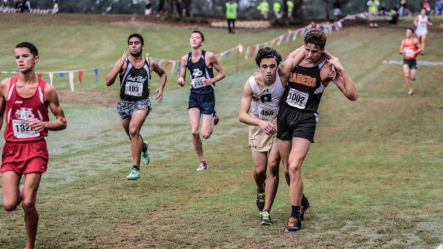 Cross country runner helps competitor cross finish line