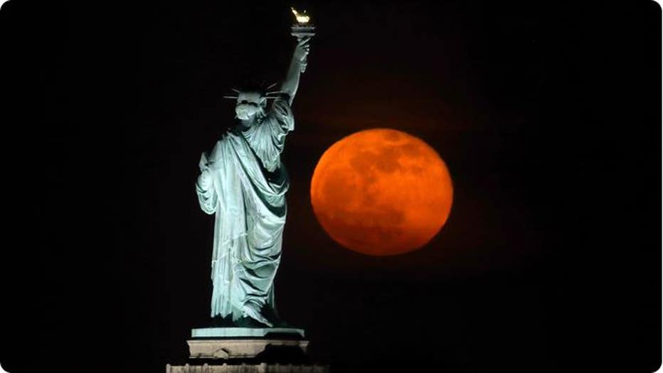 FILE - The pink moon rises next to the Statue of Liberty in New York City a day after being full on April 27, 2021 as seen from Jersey City, New Jersey. (Gary Hershorn / FOX Weather)