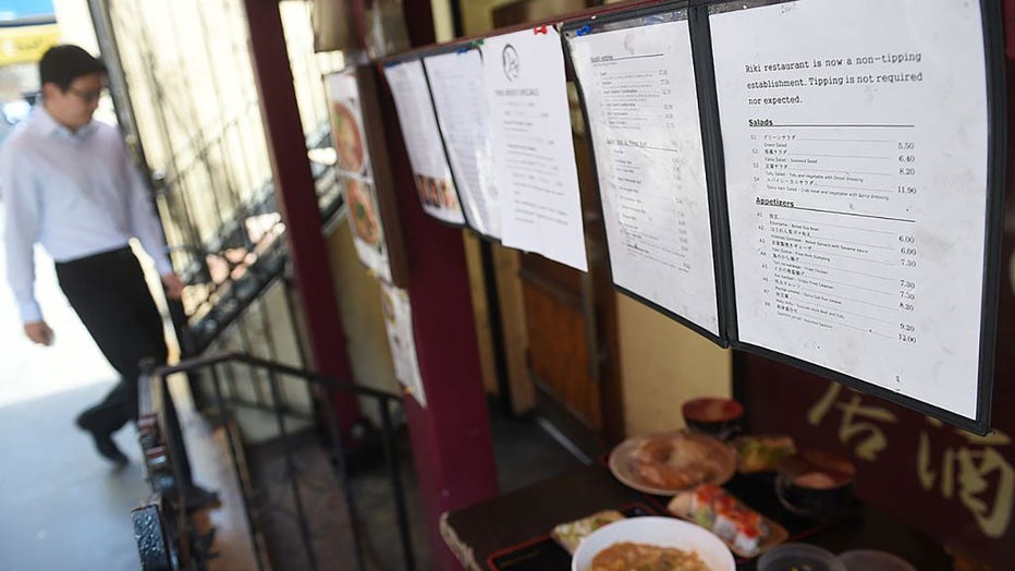 FILE - A menu displays a non-tipping policy in front of Japanese restaurant Riki, in New York on May 1, 2014. (Photo credit: EMMANUEL DUNAND/AFP via Getty Images)