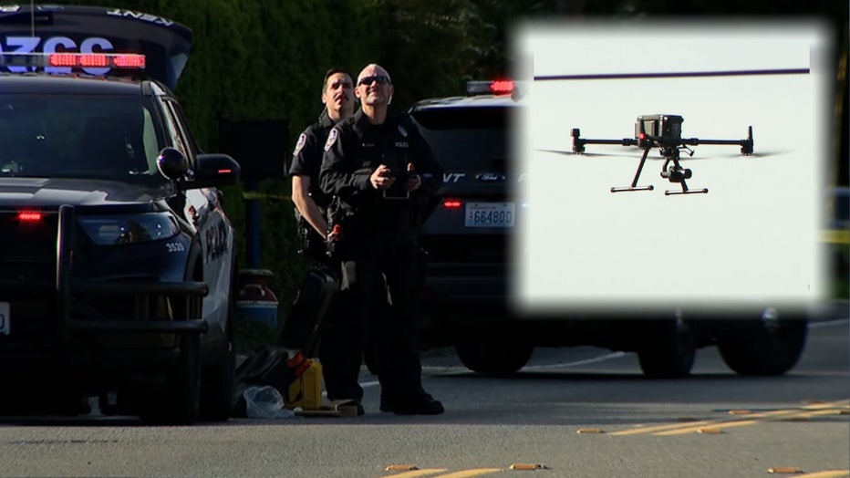 photo of officers standing next to their police cruisers at the scene of a crash. the officers can be seen holding a remote control to operate a drone.