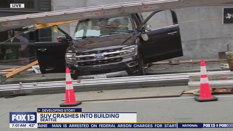 photo of a car that crashed into a building in downtown seattle monday morning. Scaffolding can be seen on top of he black SUV, which has both of its passenger doors open.