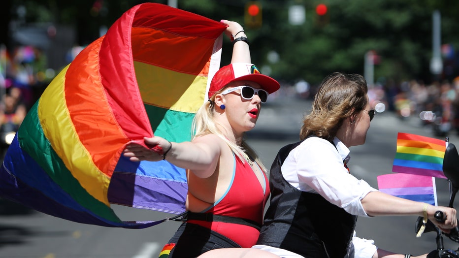 woman waves pride flag on back of motorcycle