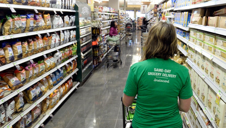 8c562c1b-Kaitlin Myers a shopper for Instacart studies her smart phone as she shops for a customer at Whole Foods in Denver.